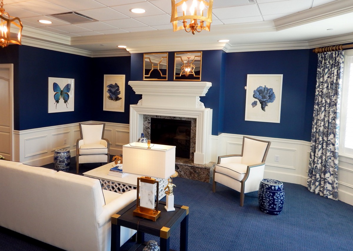 A modern living room featuring blue walls, white furniture, and elegant artwork, centered around a cozy fireplace.