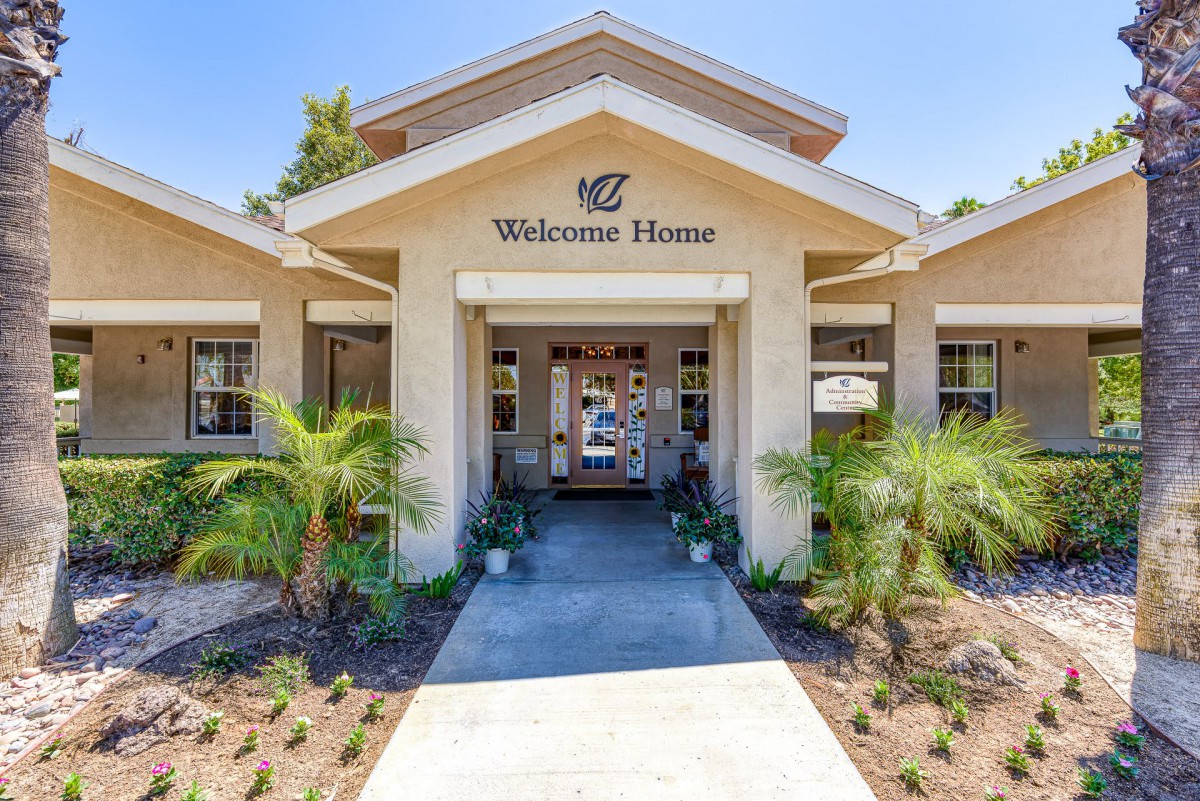 A welcoming entrance to a residential building with palm trees and neat landscaping.