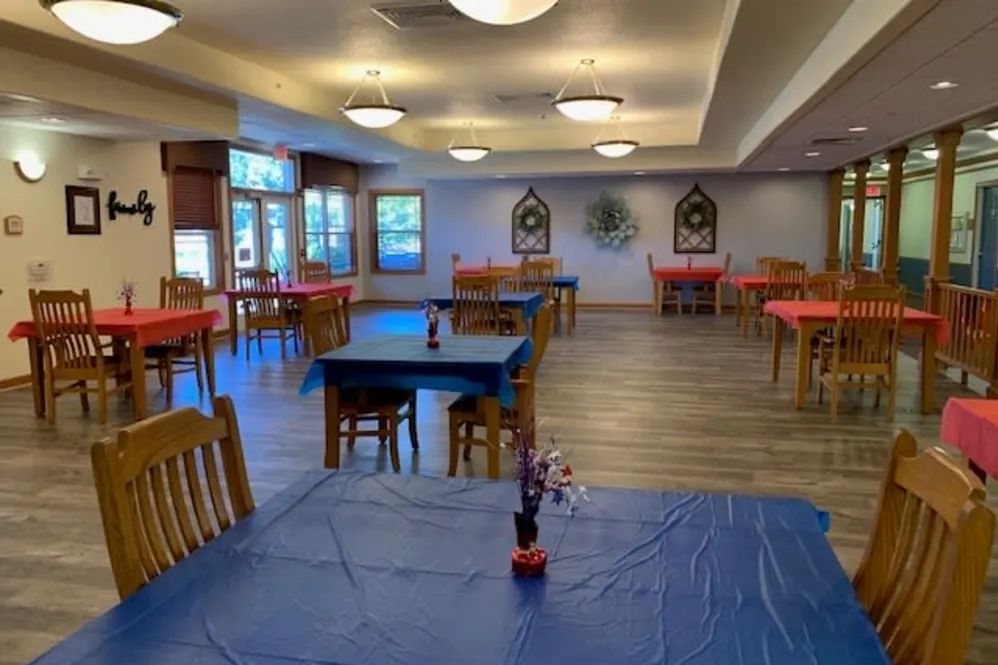 An empty dining room with tables covered in colorful tablecloths and simple decorations.