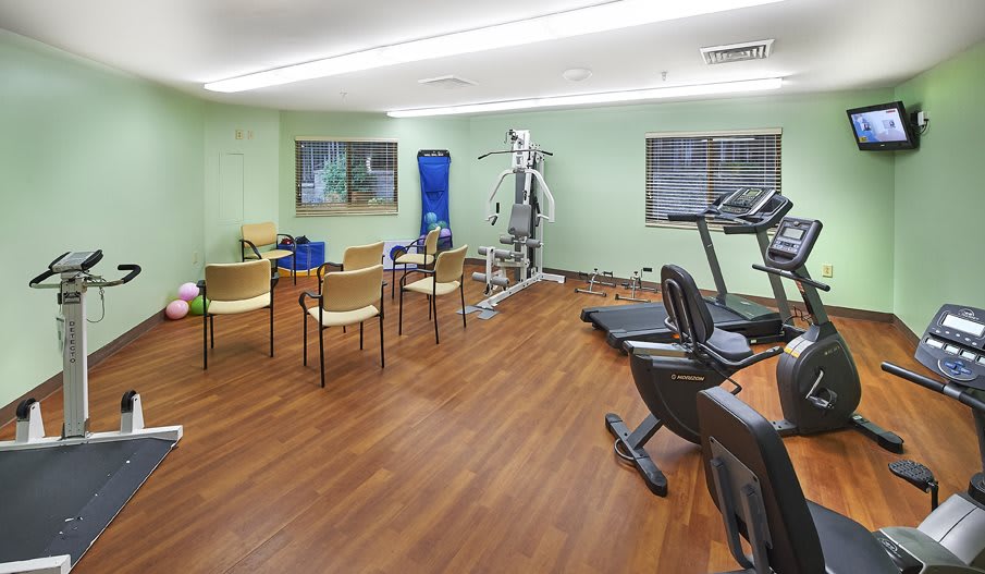A small gym with fitness equipment and chairs arranged in a clean, indoor setting.