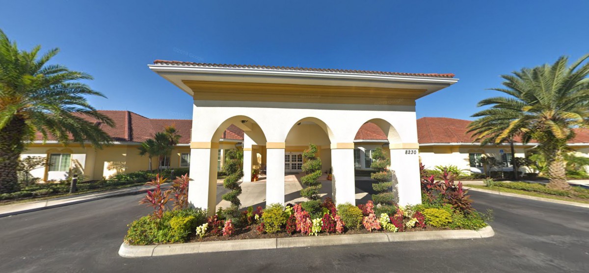 A sunny view of a building entrance with arches and vibrant landscaping.