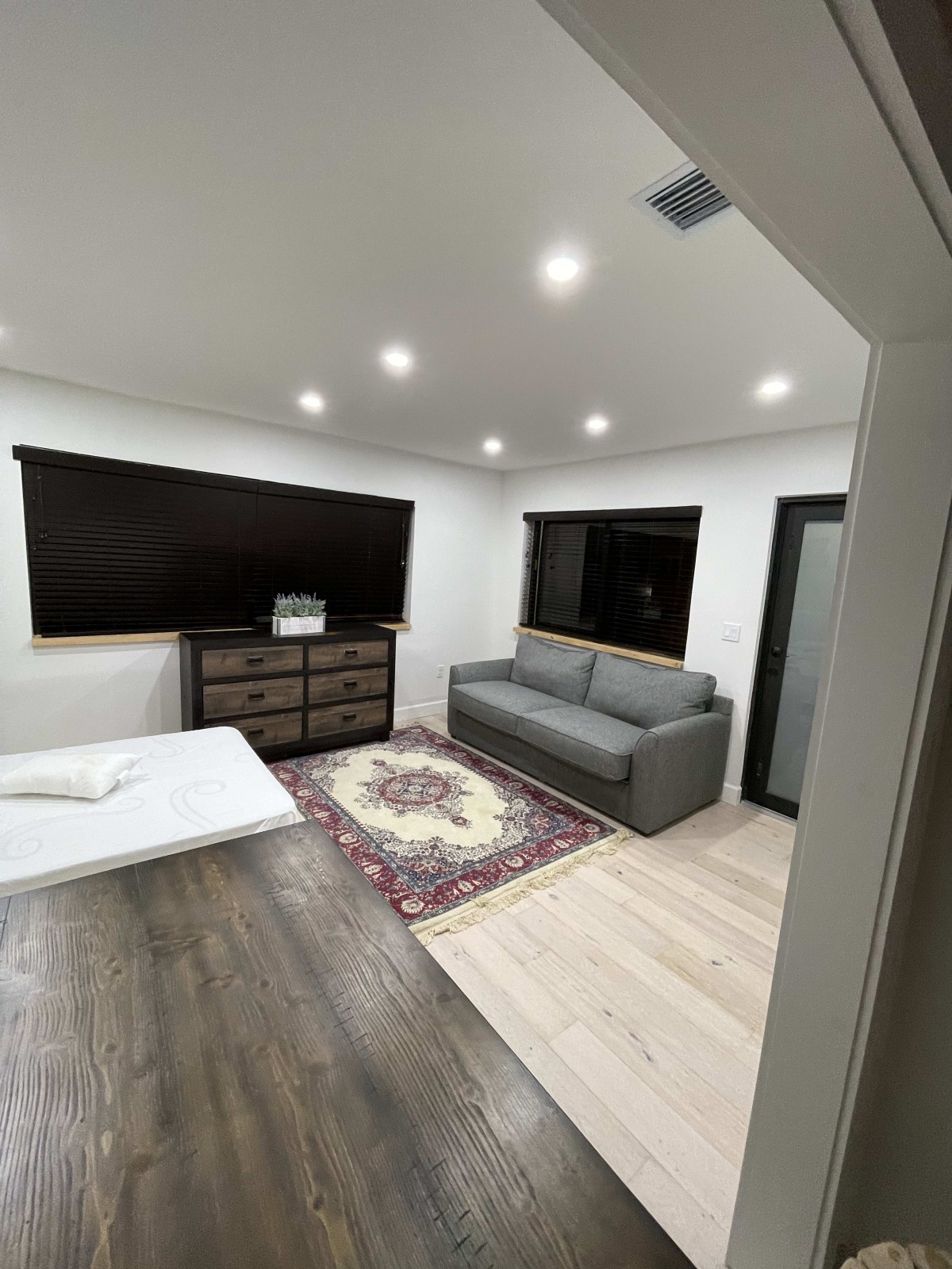 A modern living room with a sofa, dresser, and rug under recessed lighting.