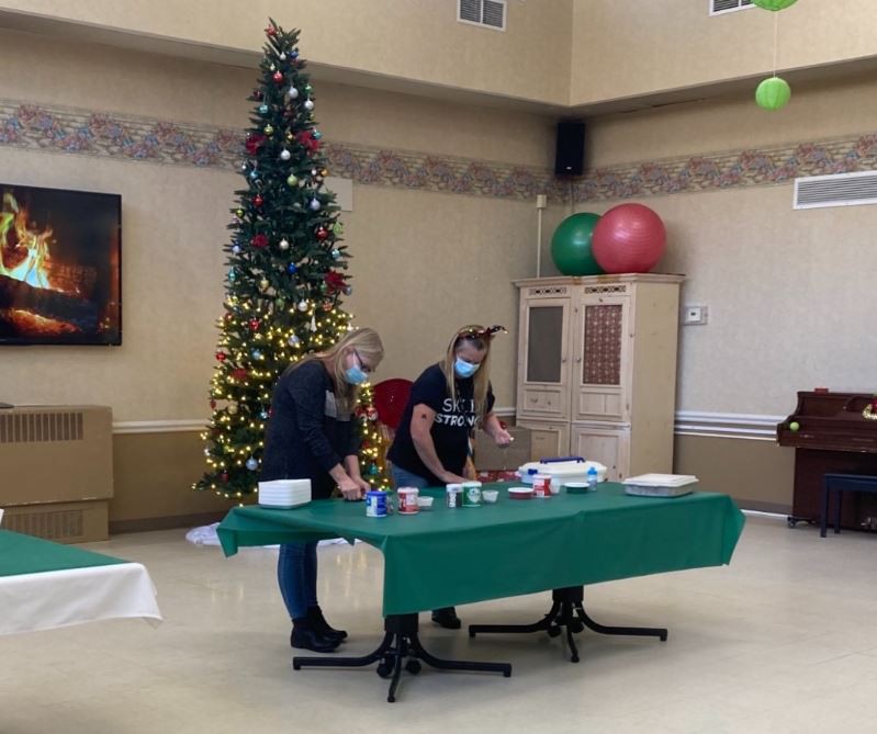 Two people wrapping gifts at a table with a decorated Christmas tree in the background.