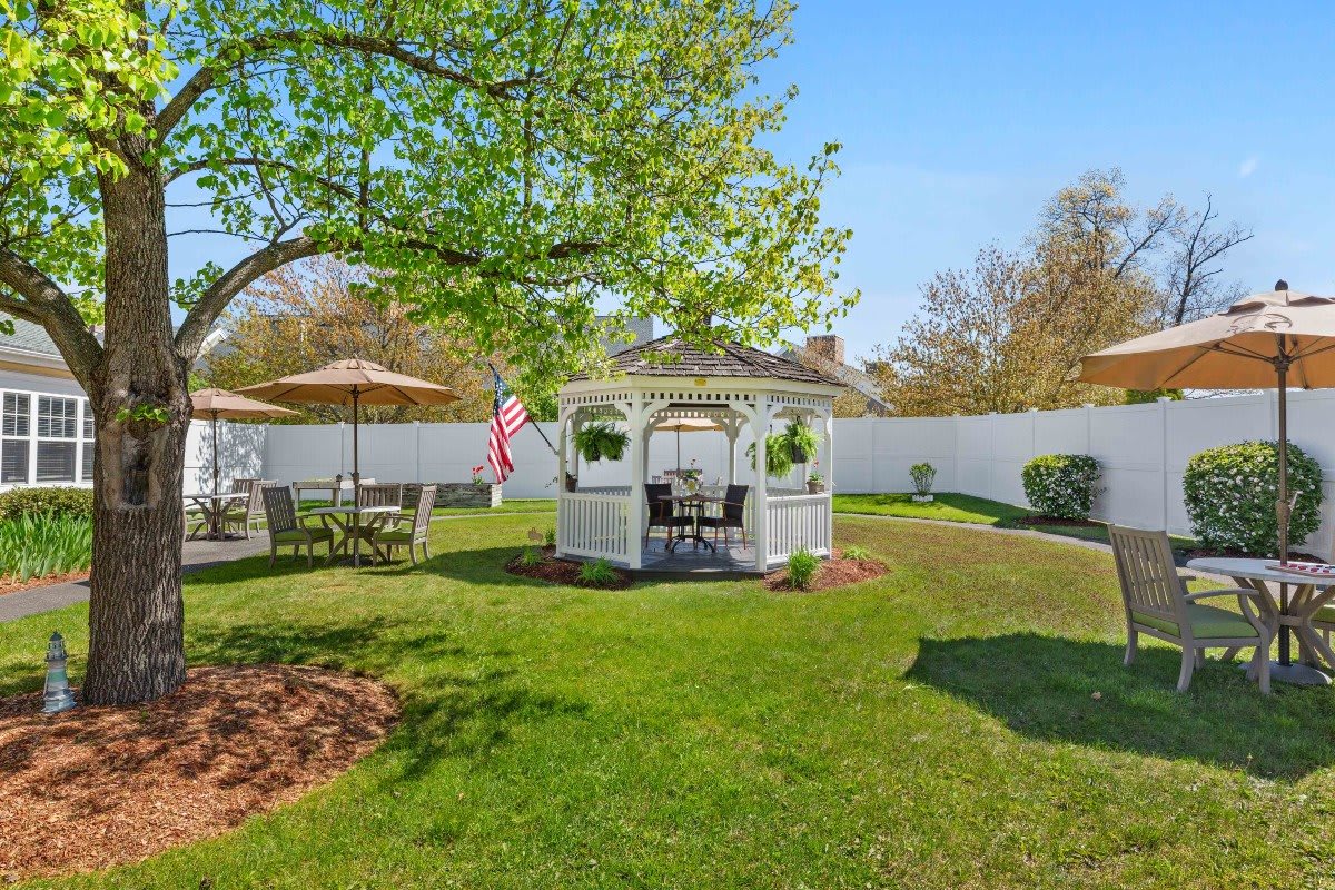 A peaceful garden with a gazebo surrounded by lush greenery and outdoor seating.