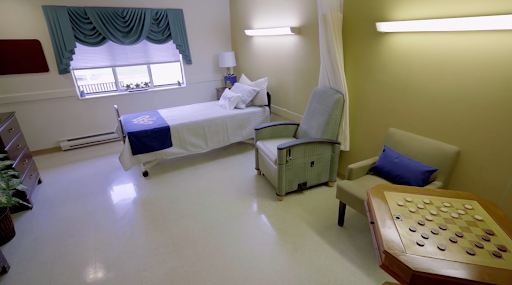A clean and minimalist hospital room featuring a bed, an armchair, and natural light.