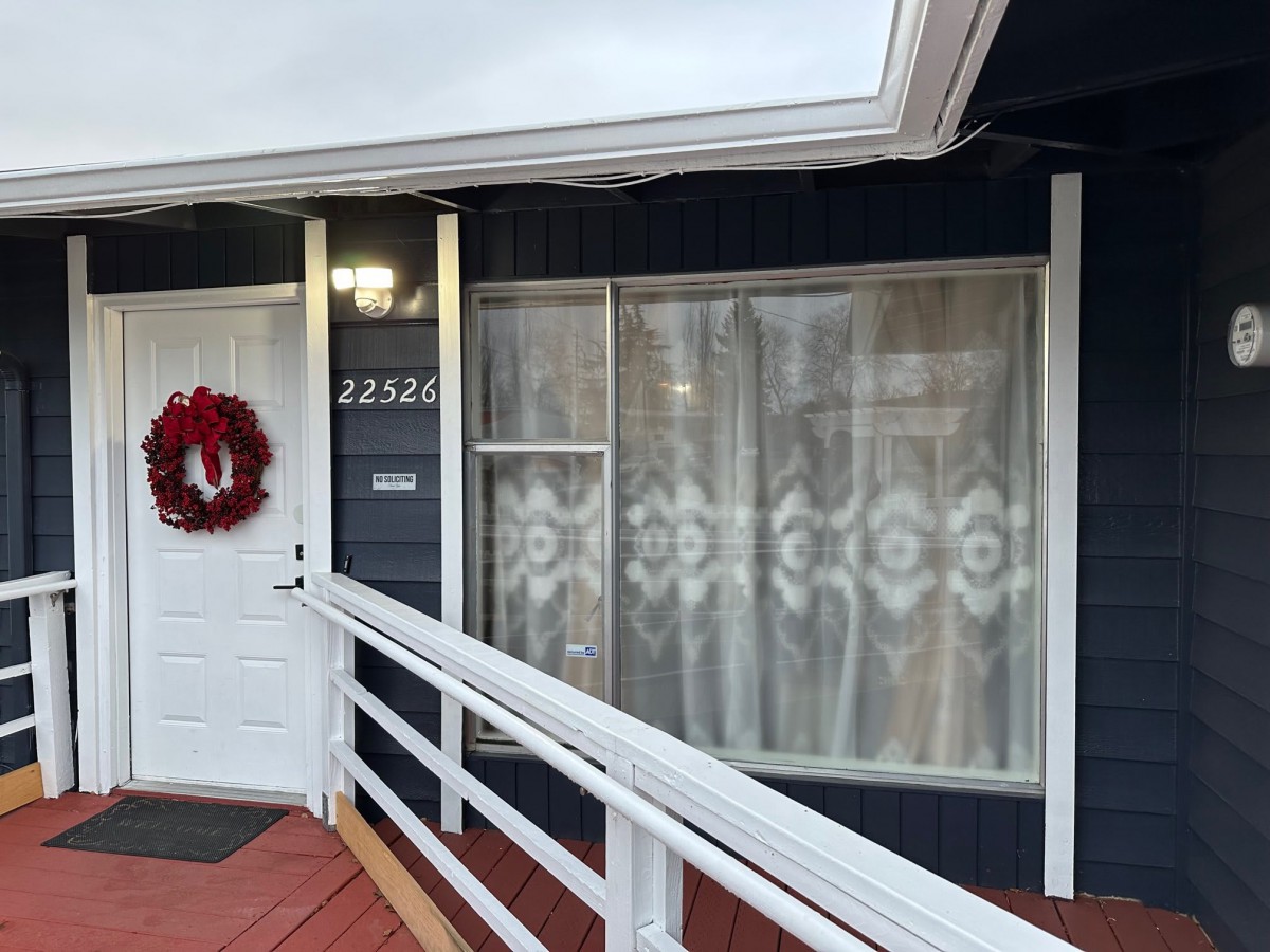 A house exterior featuring a white door with a red wreath, adjacent window with curtains, and an access ramp.