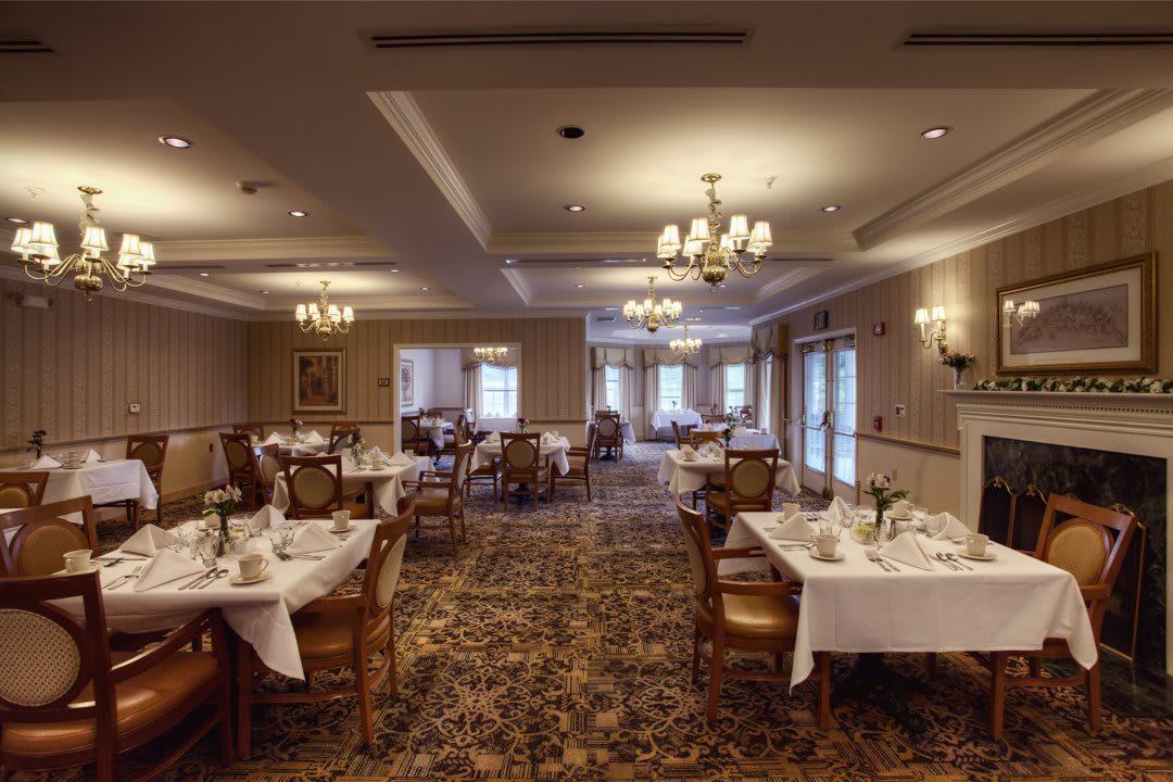 An elegant dining room with neatly arranged tables and chairs, adorned with chandeliers and a carpeted floor.