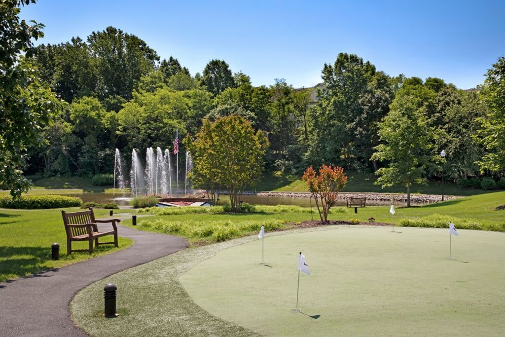 A scenic park area featuring a small golf course, fountain, and lush greenery.