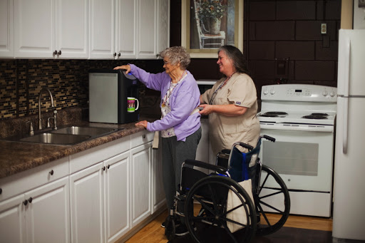 A caregiver assists an elderly woman in the kitchen while a wheelchair is nearby, highlighting the importance of support and independence.