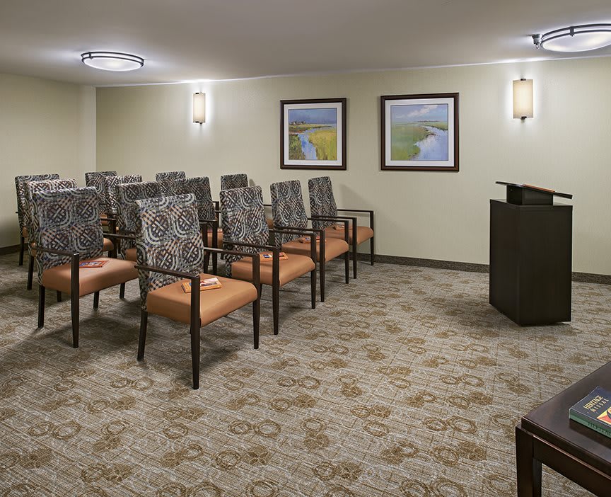 A neatly arranged meeting room with rows of chairs facing a podium and framed artwork on the walls.