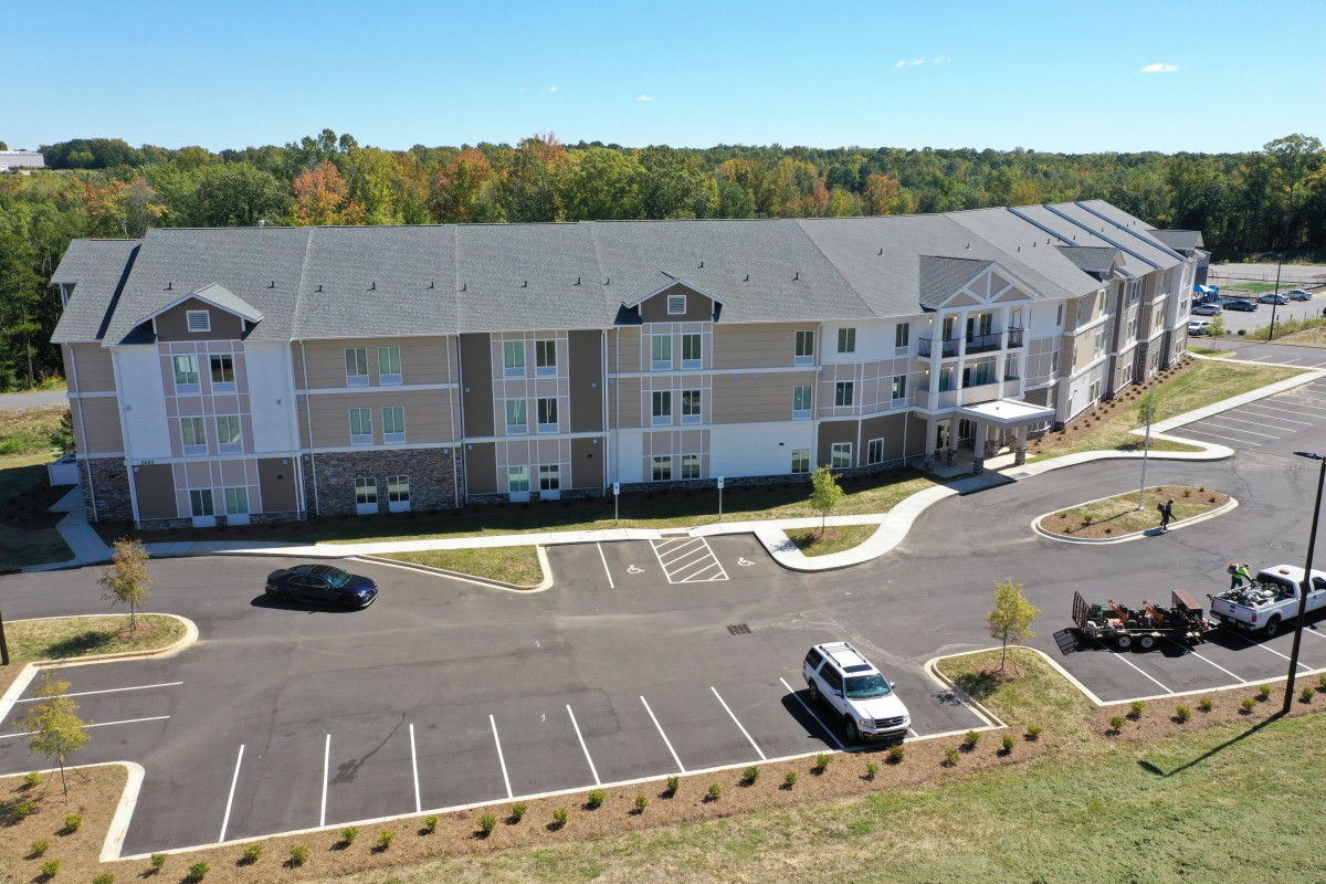 Aerial view of a suburban apartment complex with a parking lot and surrounding greenery.