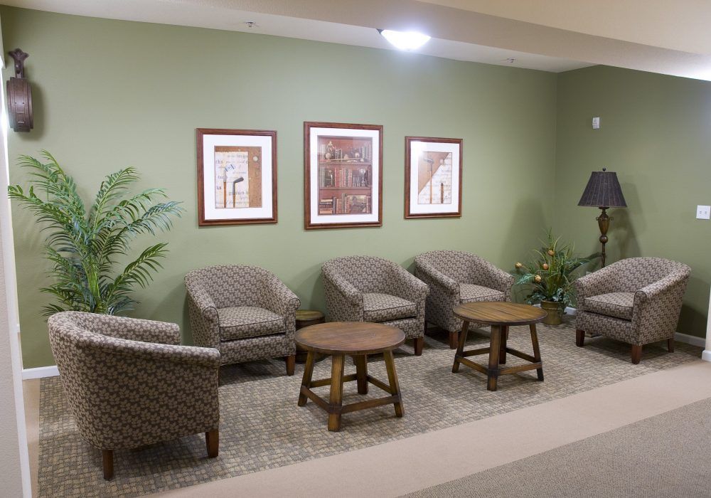 A cozy waiting area with comfortable chairs, small tables, and decorative paintings on a green wall.