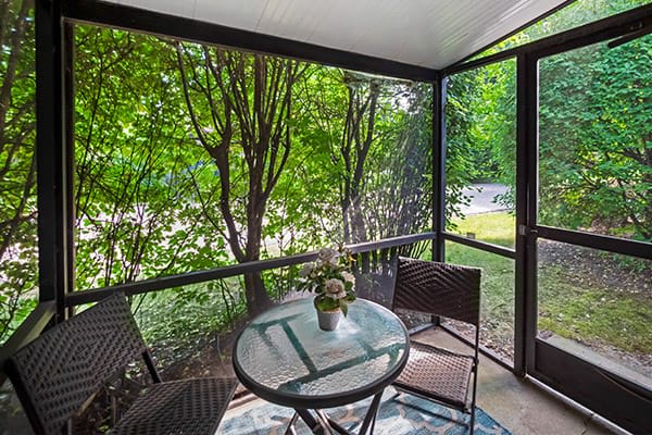 A cozy screened porch with a glass table and chairs surrounded by lush greenery.