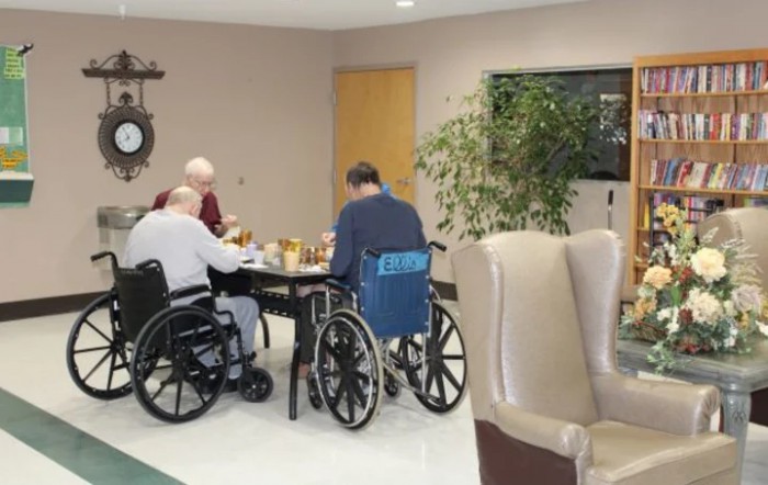 Elderly individuals in wheelchairs having a meal together in a care home setting.