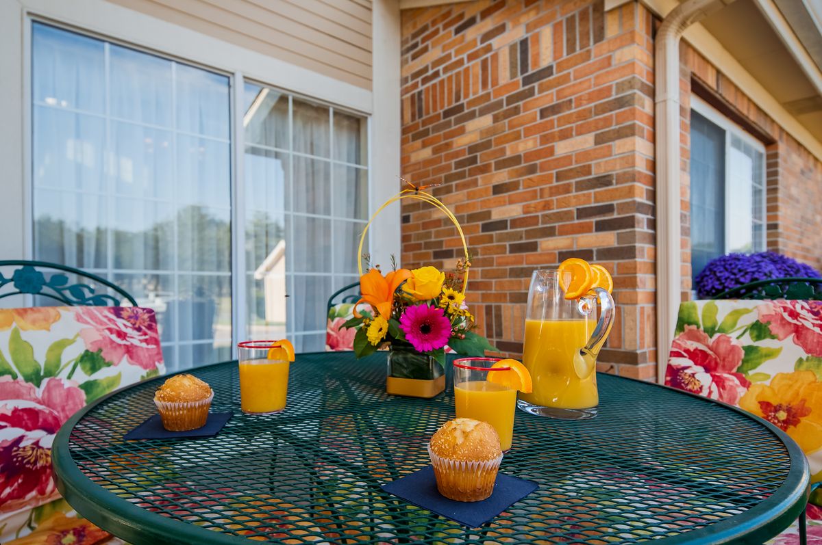 A cozy outdoor breakfast setup with orange juice and muffins on a patio table, complemented by a vibrant flower arrangement.