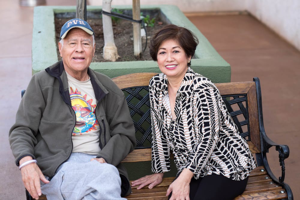 A man and a woman sitting together on a bench outdoors.
