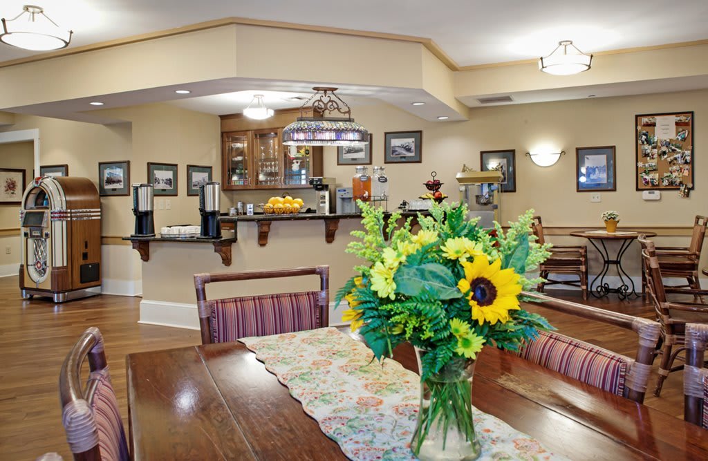 A cozy dining area with a table adorned by a bouquet of sunflowers, leading to a well-equipped kitchen in the background.
