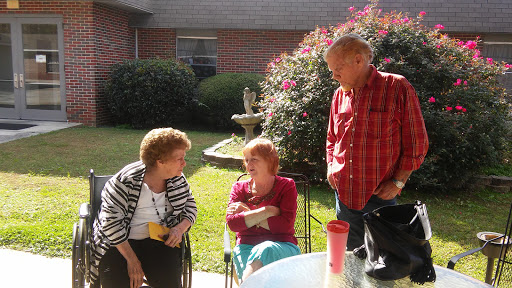 A group of three people engaged in conversation outdoors, enjoying a sunny day in the garden.