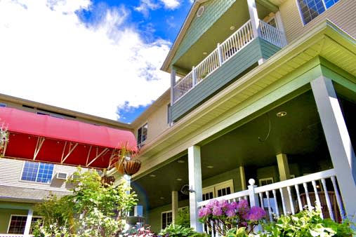 A two-story house featuring balconies and a vibrant garden under a blue sky.