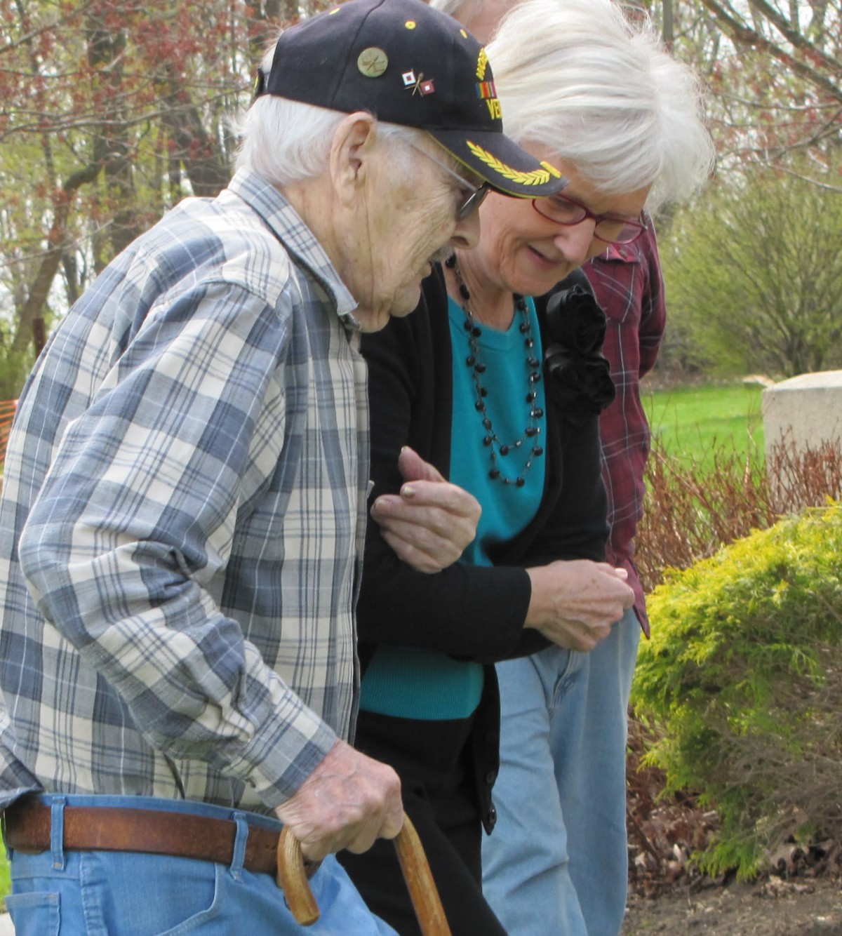 Two elderly individuals walking outdoors with support.