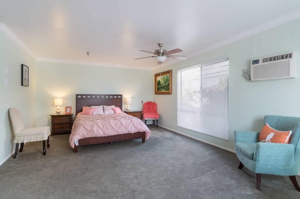 A spacious bedroom with modern decor, featuring a bed, chairs, and large windows.