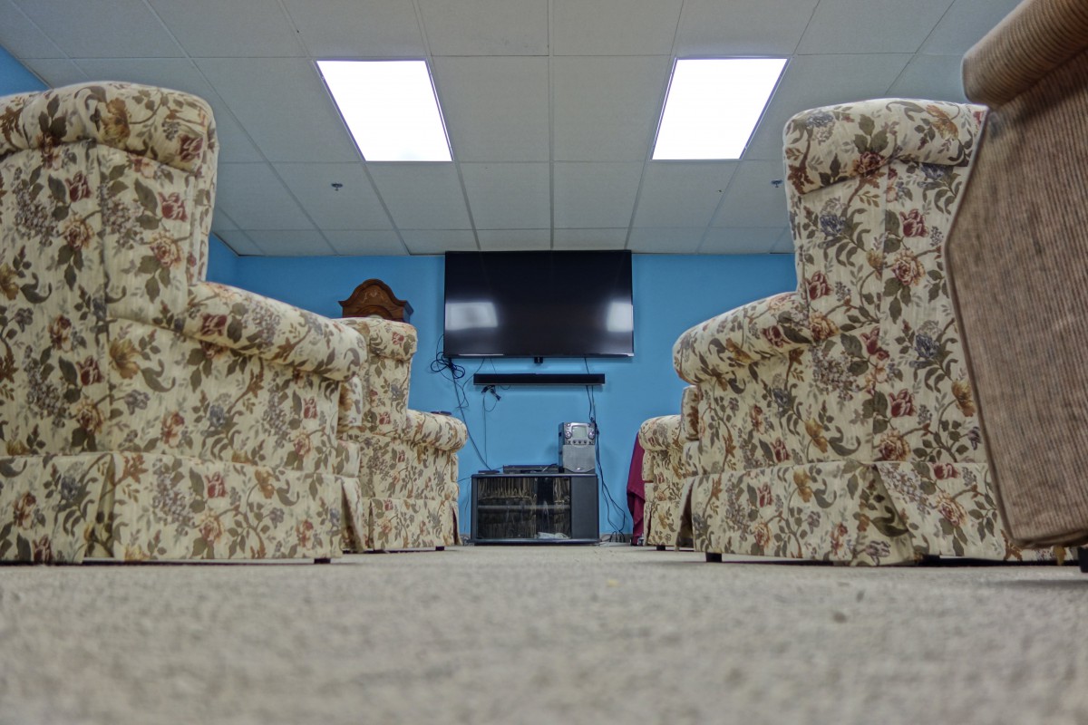 A living room setup with floral armchairs, a carpeted floor, and a wall-mounted television.