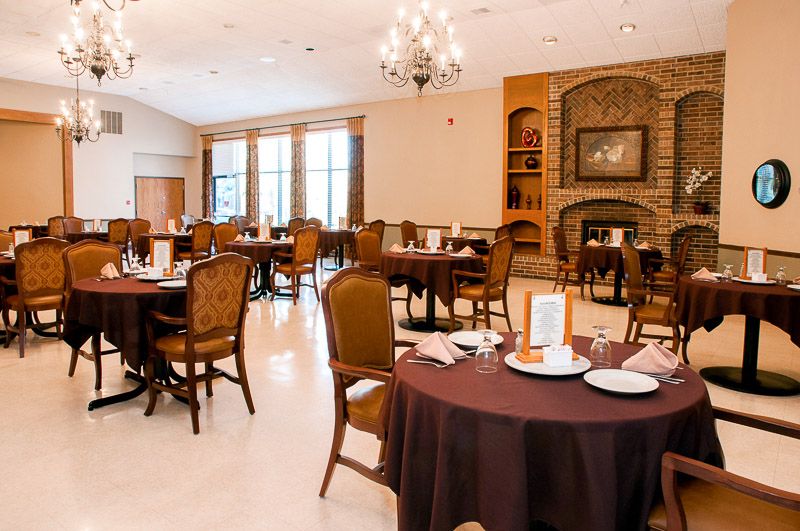 An elegant dining room featuring neatly arranged tables and chairs, with large windows and a cozy fireplace.