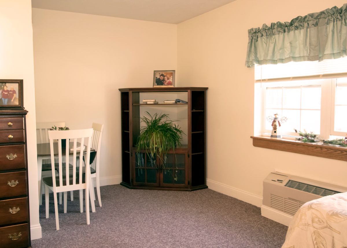 A cozy room with a dining area, featuring a corner shelf and window.