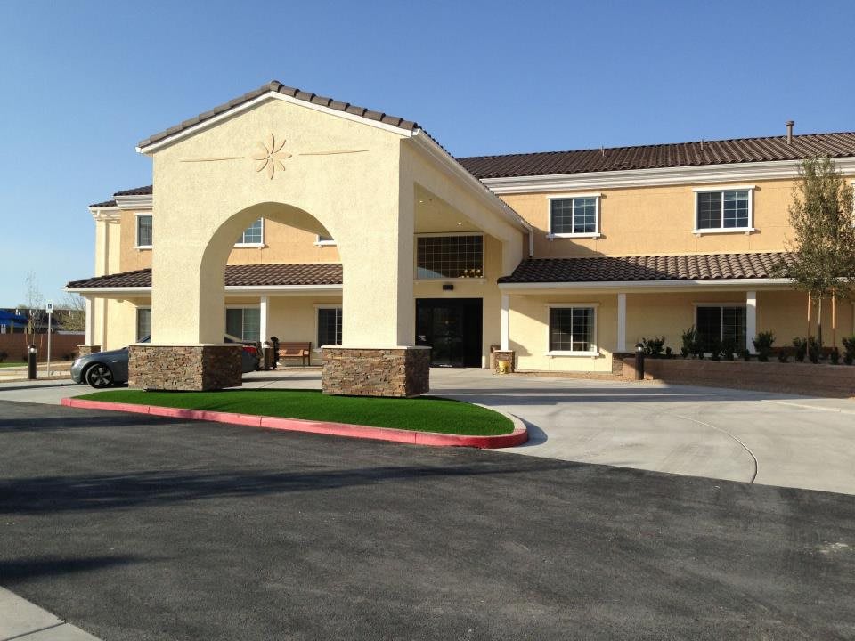 A two-story hotel building with a large entrance and surrounding parking area on a sunny day.