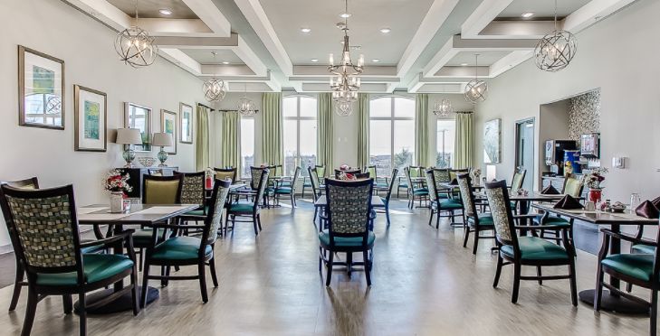 An elegantly designed dining room with multiple tables and chairs, featuring chandeliers and large windows with curtains.