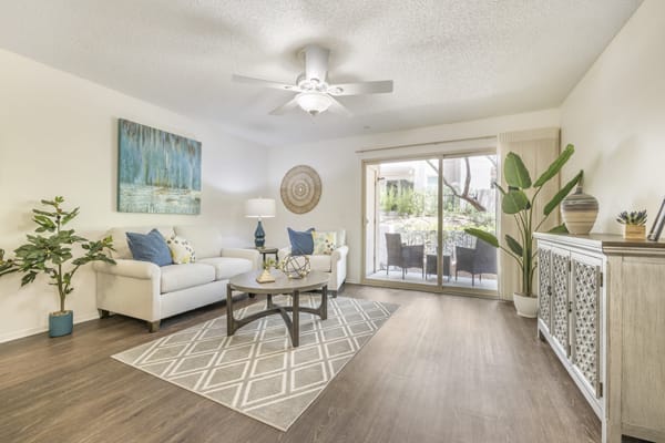 A modern living room with stylish furniture and decor, featuring a cozy sofa, coffee table, artwork, and a large plant near sliding glass doors.