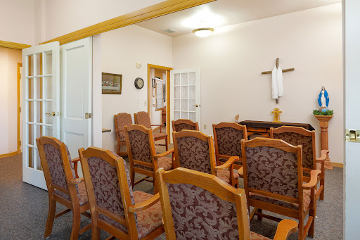 A tranquil room featuring wooden chairs arranged for reflection, highlighted by a religious cross on the wall.