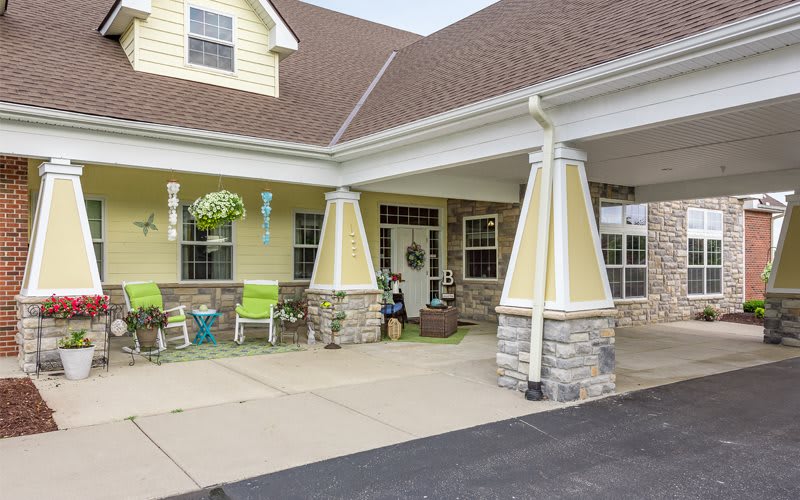 A welcoming porch with columns and stonework, featuring seating and hanging plants.