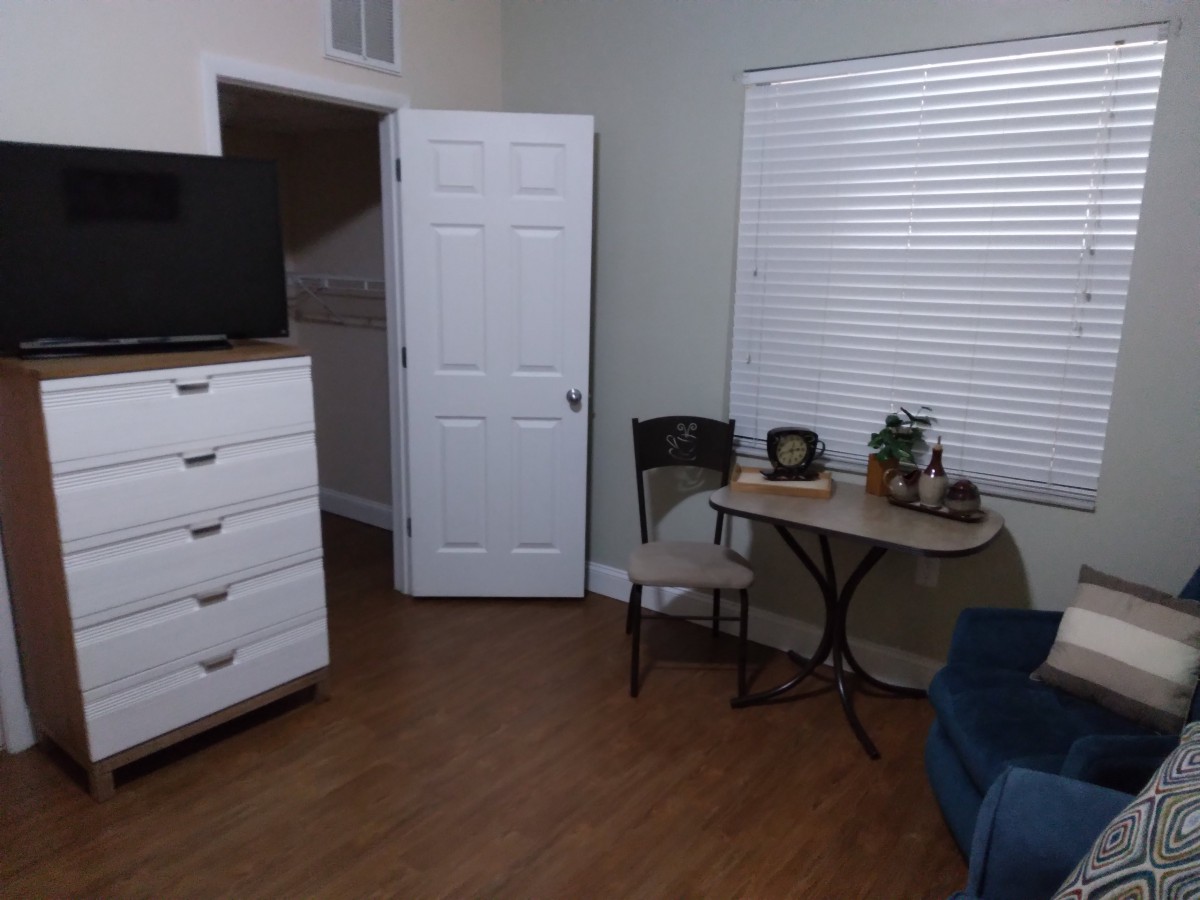 A cozy room with a dresser, TV, small table, and chairs.