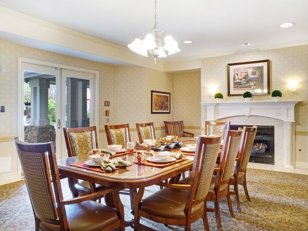 A spacious dining room with a long wooden table and elegant chairs, featuring a chandelier and a fireplace.