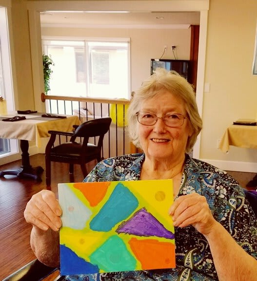 Woman proudly displaying her colorful abstract painting in an indoor setting.