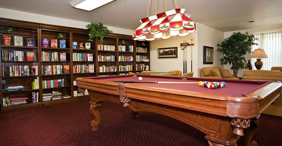 A cozy recreation room featuring a billiards table and a library with bookshelves.