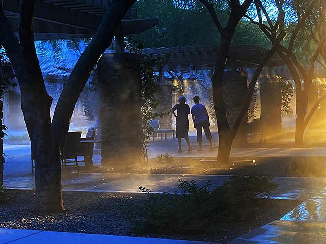 Two people walk along a misty, tree-lined path illuminated by blue lighting.