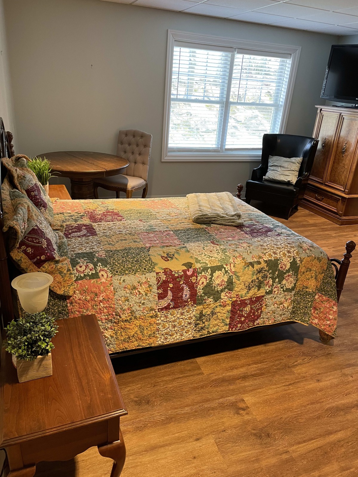 A cozy bedroom featuring a colorful quilt on the bed, with hardwood flooring and classic furniture.