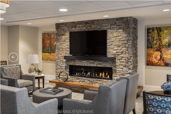 A modern living room features a stone fireplace with a mounted television and cozy seating.
