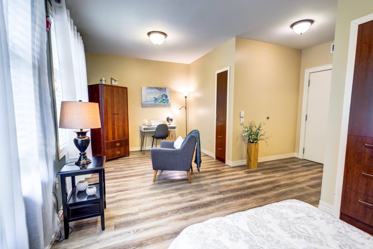 A cozy bedroom with a desk and chair next to a wardrobe, featuring warm lighting and stylish flooring.