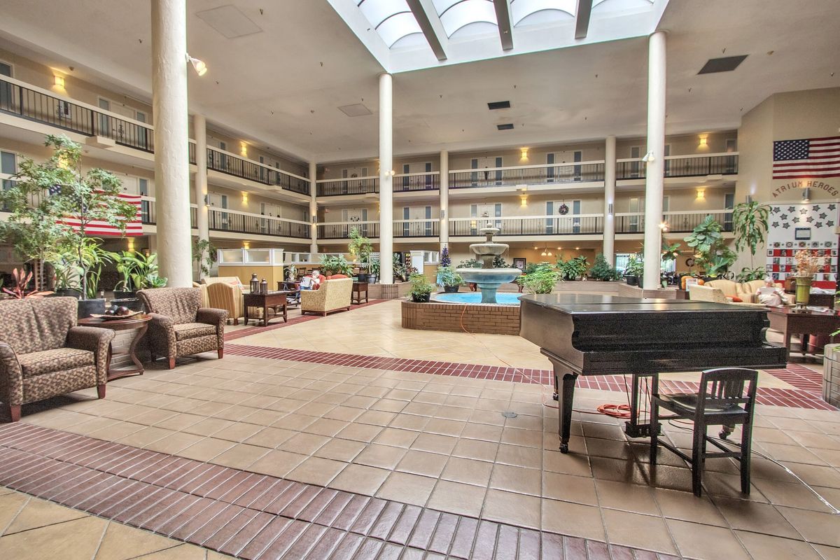 A spacious hotel lobby featuring a piano and comfortable seating under a skylight.
