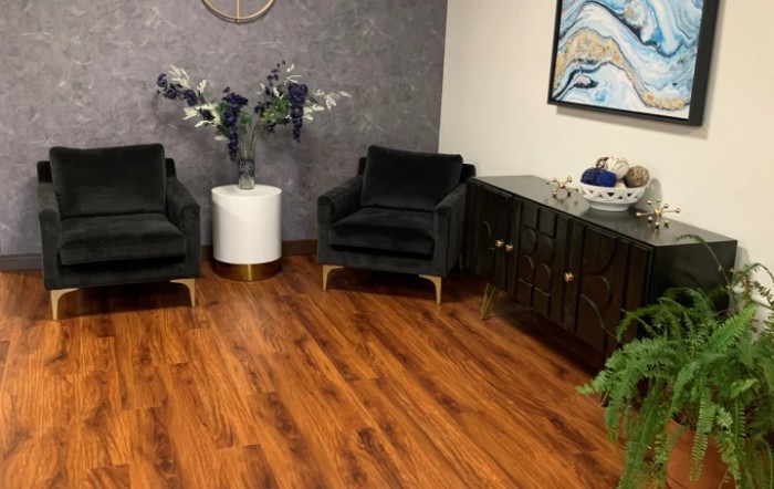 A modern office waiting area with black chairs, a white side table with floral decorations, and a dark cabinet on a hardwood floor.