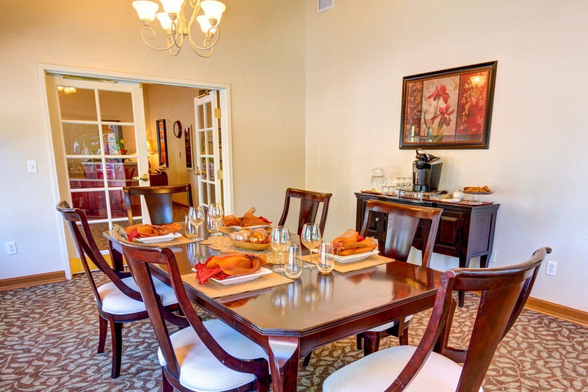 An elegantly set dining room with a polished wooden table and chairs, adorned with a chandelier and decorative artwork.