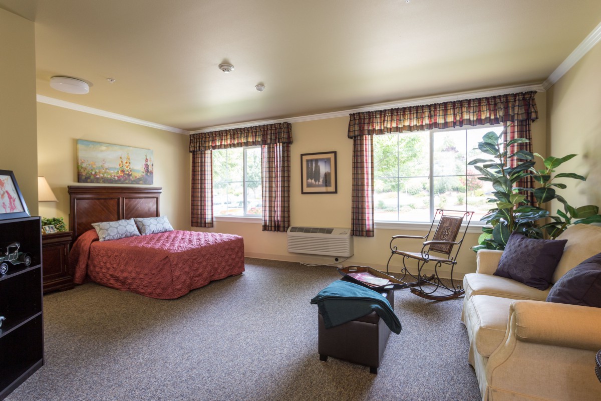 A cozy hotel room featuring a bed, an armchair, and large windows with patterned curtains.