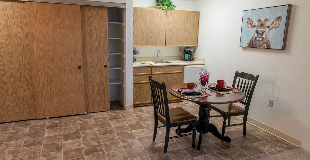 A cozy kitchen and dining area featuring wooden cabinets, a small round table set with dishware, and a pantry with sliding doors.