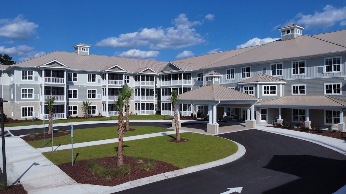 A modern residential building with a landscaped driveway and palm trees under a clear blue sky.