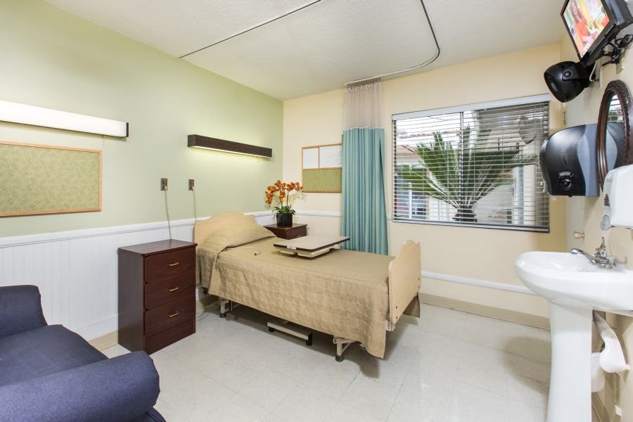 A clean and well-organized hospital room with a single bed and natural lighting.
