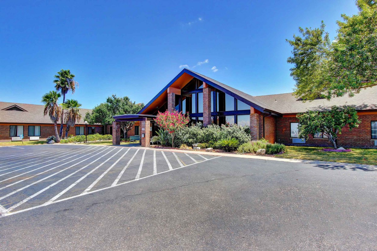 A view of a modern building with a large parking lot under a clear blue sky.