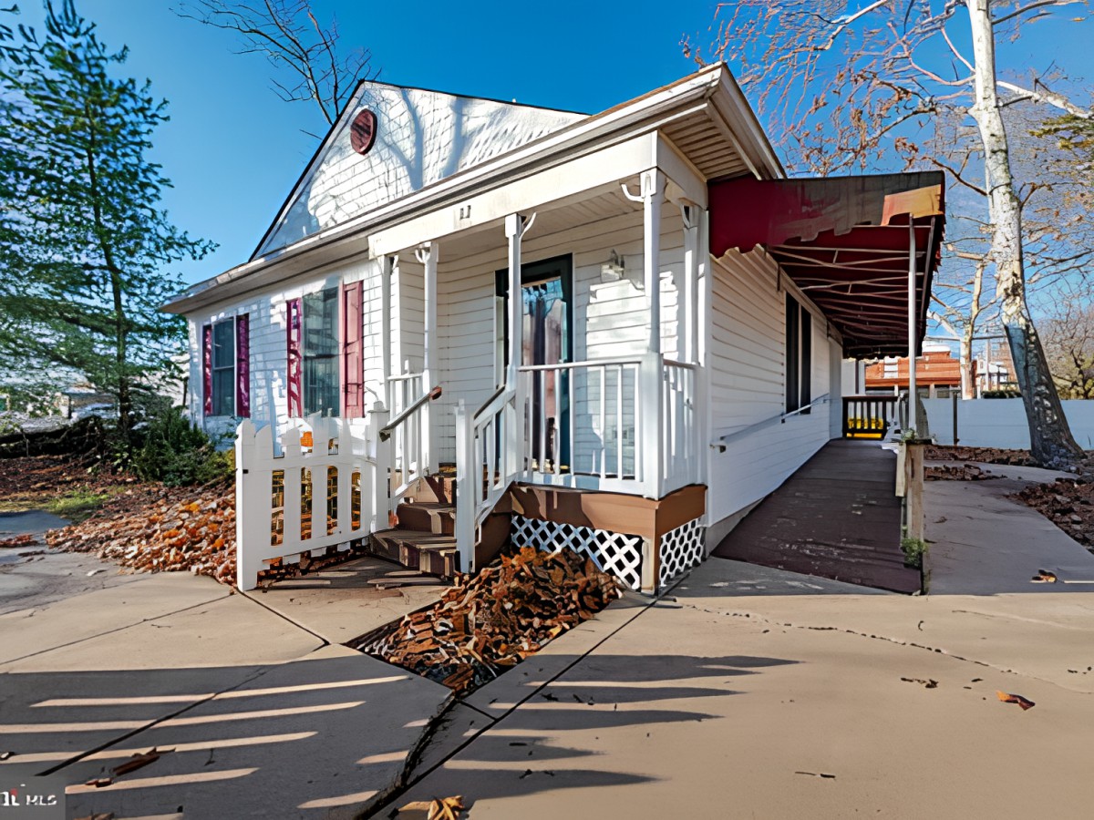 A small white house with a porch and a ramp, surrounded by fallen leaves on an autumn day.